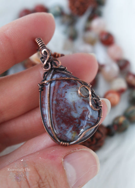 Longing for the serenity of a forest walk? Let the Amanita Forest Mala carry you away. Hand-knotted with Flower Agate, Brecciated Red Jasper, Rainforest Jasper, Smoky Quartz, and 4 Rudraksha seeds, this 72-bead mala necklace is designed to help nature lovers, energy healers, and nature witches ground themselves and open their hearts to new opportunities. Crafted with a copper wire-wrapped Red Moss Agate pendant, this unique piece is the perfect companion for your meditation practice. Beaded Mala