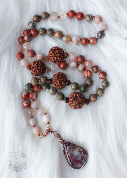 Longing for the serenity of a forest walk? Let the Amanita Forest Mala carry you away. Hand-knotted with Flower Agate, Brecciated Red Jasper, Rainforest Jasper, Smoky Quartz, and 4 Rudraksha seeds, this 72-bead mala necklace is designed to help nature lovers, energy healers, and nature witches ground themselves and open their hearts to new opportunities. Crafted with a copper wire-wrapped Red Moss Agate pendant, this unique piece is the perfect companion for your meditation practice. Beaded Mala
