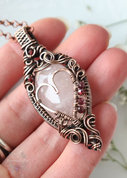 Aphrodiety pendant, a Rose Quartz and Garnet copper wire-wrapped jewelry piece with a filigree design and a handmade copper heart. Rose Quartz center with faceted Garnet beads, embodying the goddess Aphrodite's essence of love and healing energy.