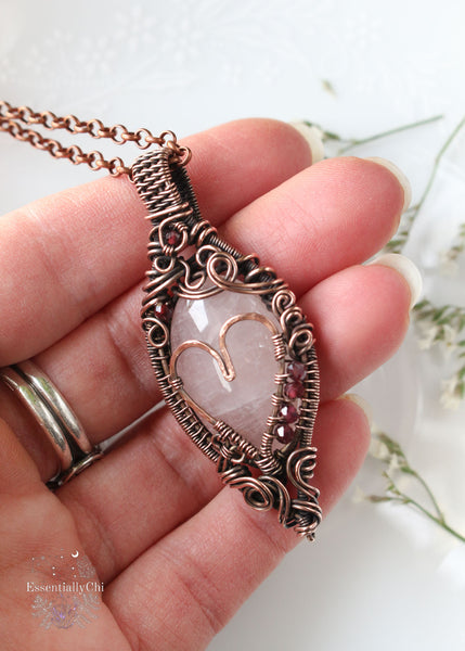 Aphrodiety pendant, a Rose Quartz and Garnet copper wire-wrapped jewelry piece with a filigree design and a handmade copper heart. Rose Quartz center with faceted Garnet beads, embodying the goddess Aphrodite's essence of love and healing energy.