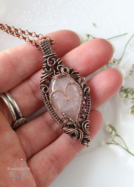 Aphrodiety pendant, a Rose Quartz and Garnet copper wire-wrapped jewelry piece with a filigree design and a handmade copper heart. Rose Quartz center with faceted Garnet beads, embodying the goddess Aphrodite's essence of love and healing energy.