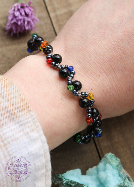 Handknotted beaded boho bracelet with nylon thread in the color grey. Gemstones are Black onyx. Seed beads are in an S curve on one side or the other of the gemstone in the color hematite color and a rainbow of color ROYGB, Silver plated hook clasp.