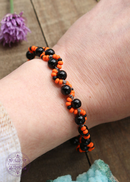 Handknotted beaded boho bracelet with nylon thread in the color grey. Gemstones are black onyx. Seed beads are in an S curve on one side or the other of the gemstone in the color Bright orange and black, Silver plated hook clasp.