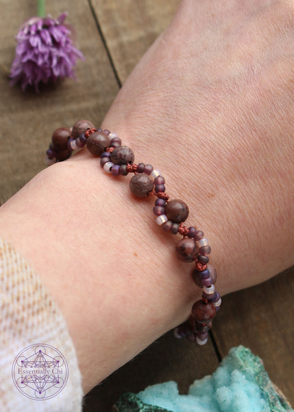 Handknotted beaded boho bracelet with nylon thread in the color dusty red. Gemstones are Mauve brecciated jasper. Seed beads are in an S curve on one side or the other of the gemstone in the color Translucent dark purple and clear, Copper hook clasp.