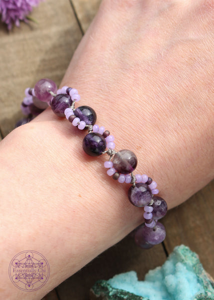 Handknotted beaded boho bracelet with nylon thread in the color lavender. Gemstones are Purple Fluorite from light to dark. Seed beads are in an S curve on one side or the other in the color light translucent purple and dark dusty purple. Silver plated hook clasp