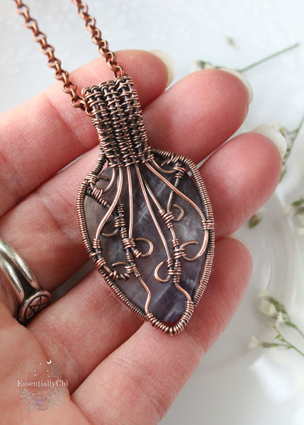 Athena pendant, a Chevron Amethyst and Rainbow Moonstone copper wire-wrapped jewelry piece with filigree details. Chevron Amethyst criss-cross design on the front, symbolizing Athena's strategic strength, and a blue flash Rainbow Moonstone in the bail. Back features intricate filigree for security and elegance, reminiscent of Athena's wisdom and warrior spirit.