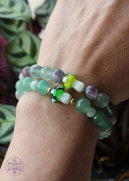 Two Crystal stretch bracelets shown on wrist. One with a dark green mushroom paired with green fluorite and amazonite beads. The other a lime green mushroom with green and purple fluorite.