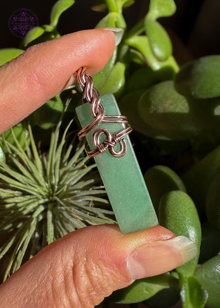 Green Aventurine Copper wire wrapped necklace with a a simple design in the front that looks like hands clasping together and has a braided bail. Hangs on a black cotton wax cord. Shown in the sun to bring out the green in the aventurine.