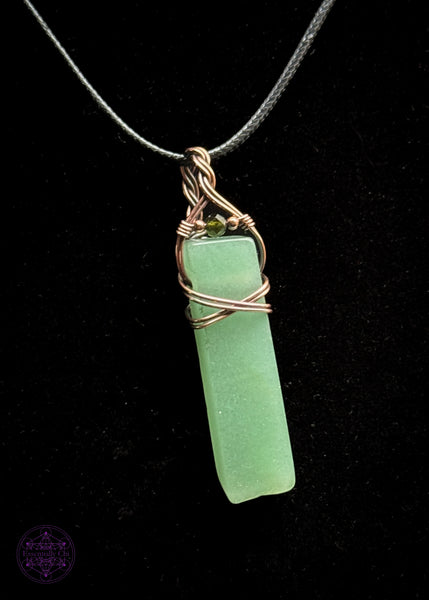 Green adventurine rectangular style pendant with a simple wrap of a criss cross over the face of the stone and a braided bail. an added green tourmaline stone is at the base of the bail. hung on a 22" black nylon cord. Shown on a black background to see details.