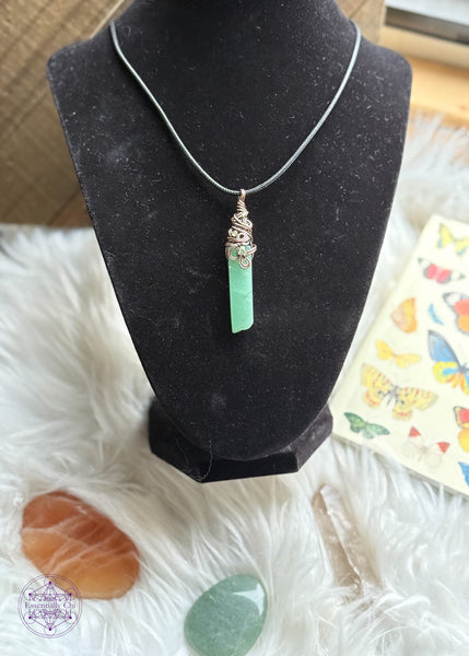 Green Aventurine rectangular crystal wrapped in copper wire around the bail with a swirly filagree design and peridot accent crystals placed within the design. Placed on a black velvet bust to shown how it hangs while worn.