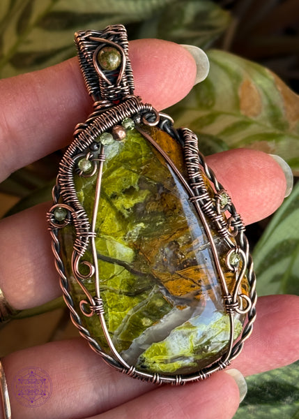 Large green opal flat palmstone wrapped in copper wire with accent stones of 2mm faceted peridot crystals and an unakite crystal in the bail. 2.75" in length and hangs from a copper ball chain. Not very heavy. Held in hand to show size and details up close. The green opal has earthy greens and browns throughout and a vein of quartz running thru the bottom.