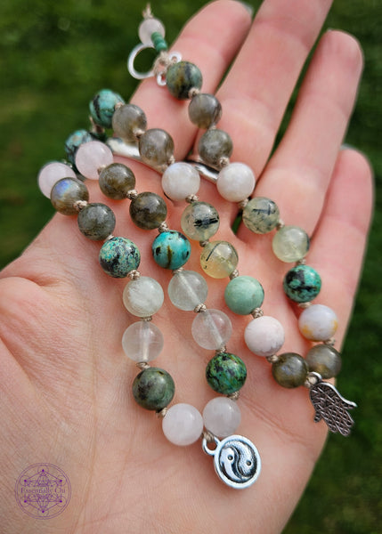 Hand-knotted beaded boho bracelets in a pastel pink and green theme. One bracelet has a in yang charm and the other has a hamsa hand charm. Beads are knotted with a sand colored nylon thread with crystals such as rose quartz, African turquoise, green fluorite, labradorite, flower agate, and prehnite. Clasp is a silver plated hook closure. Shown in hand for comparison.