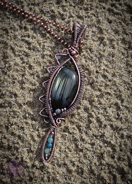 Copper wire wrapped necklace with an oval labradorite that has lines of yellow, green and blue flashes like the Norther Lights. On the left side there is a zig zag pattern with faceted rainbow moonstone bead with blue flash. The zig zag makes the pendant look like an eye when held sideways. At the base of the pendant is a long oval loop that encases small faceted smoky quartz and green tourmaline beads. Theres a copper coiling up the right side and copper accent beads throughout, truly a statement piece!