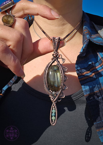 Copper wire wrapped necklace with an oval labradorite that has lines of yellow, green and blue flashes like the Norther Lights. On the left side there is a zig zag pattern with faceted rainbow moonstone bead with blue flash. The zig zag makes the pendant look like an eye when held sideways. At the base of the pendant is a long oval loop that encases small faceted smoky quartz and green tourmaline beads. Theres a copper coiling up the right side and copper accent beads throughout, truly a statement piece!