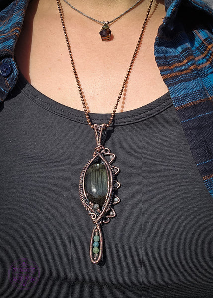 Copper wire wrapped necklace with an oval labradorite that has lines of yellow, green and blue flashes like the Norther Lights. On the left side there is a zig zag pattern with faceted rainbow moonstone bead with blue flash. The zig zag makes the pendant look like an eye when held sideways. At the base of the pendant is a long oval loop that encases small faceted smoky quartz and green tourmaline beads. Theres a copper coiling up the right side and copper accent beads throughout, truly a statement piece!