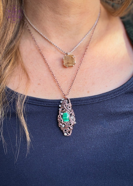 Malachite wrapped in a diamond shaped copper wire frame with a filagree design and swirls, with added accents of 2mm rainbow moonstone faceted beads. Shown worn to show how it hangs around the neck.