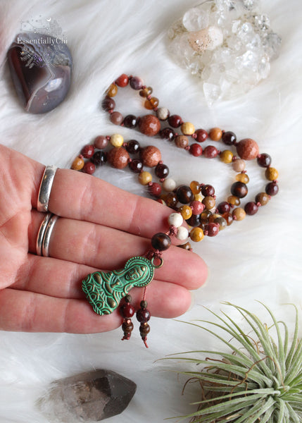 Experience divine energy with our Mookaite Crystal Beaded Mala featuring a Kwan Yin bronze pendant. Mookaite, goldstone, garnet, smoky quartz, and wood beads, meticulously crafted for those who are on a healing journey. 30" long, shorter than traditional Malas, ensuring both style and ease of wear.