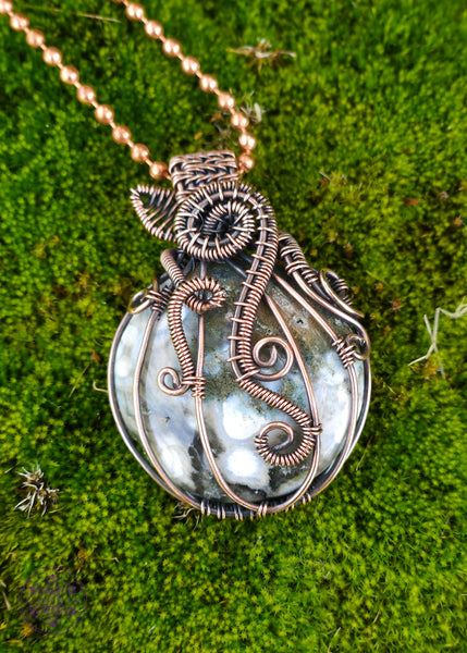 Copper wire wrapped pumpkin pendant with a green ocean jasper crystal. The white dots on the ocean jasper remind me of the warts on the warted pumpkins for this design. The bail is short to resemble a stem, and a wire wrapped leaf out the base of the stem. Vine curls around the ridges of the pumpkin.
