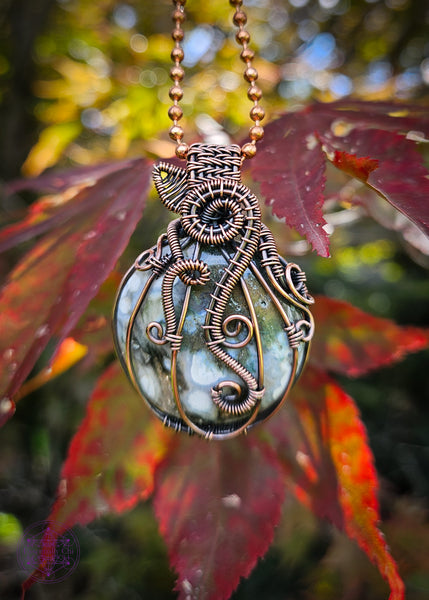 Copper wire wrapped pumpkin pendant with a green ocean jasper crystal. The white dots on the ocean jasper remind me of the warts on the warted pumpkins for this design. The bail is short to resemble a stem, and a wire wrapped leaf out the base of the stem. Vine curls around the ridges of the pumpkin.