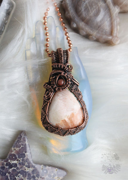 Elevate your spiritual style with our Peach Scolecite Copper Wire Wrapped Necklace. Delicately woven copper embraces a teardrop-shaped peach scolecite, accompanied by a pink jasper in the bail. This handcrafted masterpiece exudes calming energy, promoting emotional healing and spiritual upliftment. Perfect for Libra & Capricorn zodiacs, this necklace aligns with the crown and third eye chakras, fostering a sense of tranquility and connecting you to the divine feminine energy.