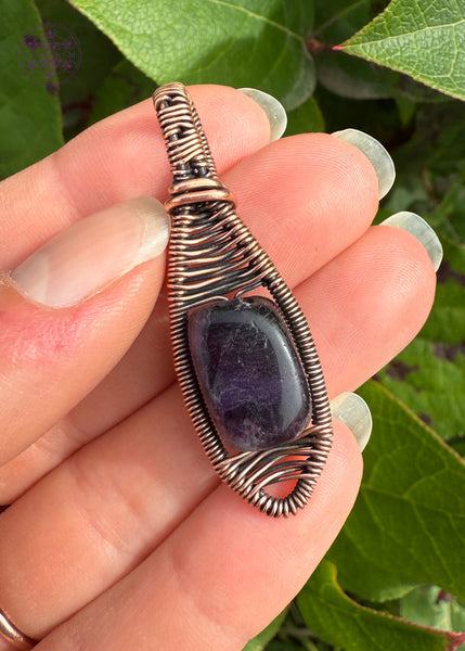 Purple Fluorite copper wire wrapped pendant in a simple minimal design. A snowshoe like shape with a deep purple rectangle bead in the center. Held in hand to show size.
