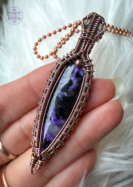 Copper wire wrapped Charoite pendant held in hand over a faux white fur. The bright light shows the detail in the stone that has some lavender chantoyancy and dark black inclusions. The bail has two faceted smoky quartz beads tucked into two triangles making this look like a galatic design.