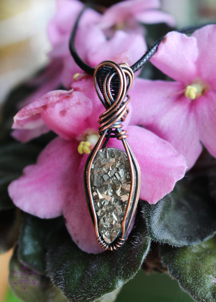 Copper wire wrapped pyrite pendant with a raw face, cubic formation. Simple wrap with double swoop along the bail. Pendant shown on an African Violet pink flower.