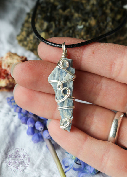 This silver plated wire wrapped pendant shown in hand for size reference has 4 swirls along the face of the blue kyanite. This raw crystal is narrow at the bottom and wider at the top. Raw Blue Kyanite Wire Wrapped Necklace for energy protection, featuring a simple, everyday wear design that enhances communication, alignment, tranquility, restful sleep, and dream recall.