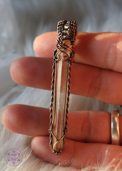 This copper wire wrapped Tangerine Singing Quartz has a twisted copper detail on the sides, and criss cross details on the bottom and at the top of the crystal.
The filagree design includes three faceted smoky quartz woven into the bail. This copper wire wrapped pendant is 2.6" in length and comes on a copper chain. shown in hand.