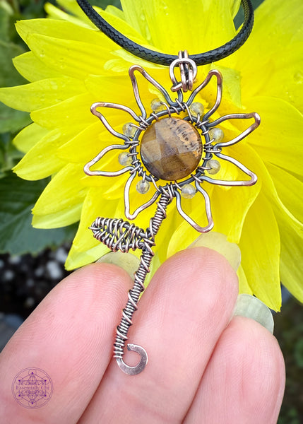 Copper wire wrapped sunflower pendant with the citrine beads as the base of each petal, and a wire wrapped stem and leaf. A rotating tiger eye bead in the center of the sunflower which shows a yellow flash in the light. Shown on hand for size reference.