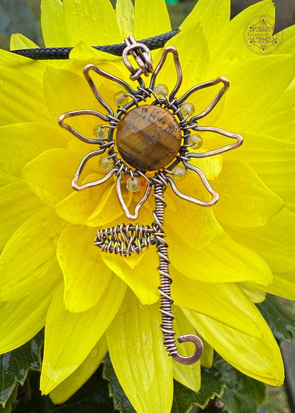 Copper wire wrapped sunflower pendant with the citrine beads as the base of each petal, and a wire wrapped stem and leaf. A rotating tiger eye bead in the center of the sunflower which shows a yellow flash in the light. Displayed on a yellow flower to show details.