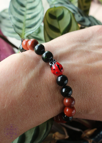 Crystal stretch bracelet with a lampwork glass lady bug focal bead, green goldstone, and red jasper beads.