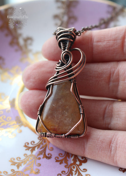 Nebu Orange Aventurine Copper Wire Wrapped Necklace - A captivating triangle-shaped pendant inspired by ancient Egyptian motifs, featuring a three-swoop bail design. The orange aventurine sparkles with golden hues, reminiscent of a radiant sunset. This handcrafted necklace, 2 inches in length, hangs gracefully from a 20-inch copper chain, symbolizing creativity, confidence, and the warm embrace of celestial energies.