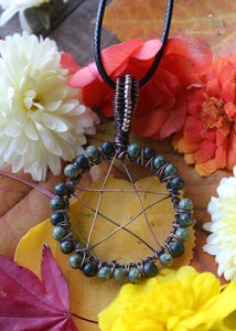 This Witchy Serpentine Pentacle Necklace features a captivating gemstone, protective pentacle, and copper wire wrap. Perfect for mystical seekers, witches, and those drawn to magical symbolism. Serpentine beads line the outside of the pentacle circle in a crisscross wire wrap design. Silver seed beads line the copper woven bail. 