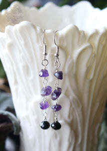 Amethyst and Black Tourmaline Dangle Earrings featuring dark purple amethyst chips and faceted black tourmaline charms. These 2.5-inch earrings hang gracefully from stainless steel ear hooks, offering a stylish blend of calming and protective energies
