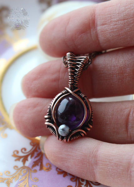 A mesmerizing Mystic Amethyst Noir Copper Necklace featuring a dark purple amethyst stone wrapped in copper wire, adorned with a dendritic opal accent bead. This handcrafted pendant hangs elegantly on an 18" copper chain, radiating spiritual energy and unique charm. Perfect for those seeking balance, tranquility, and a touch of bohemian elegance in their jewelry collection.