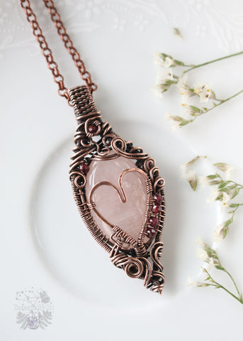 Aphrodiety pendant, a Rose Quartz and Garnet copper wire-wrapped jewelry piece with a filigree design and a handmade copper heart. Rose Quartz center with faceted Garnet beads, embodying the goddess Aphrodite's essence of love and healing energy.