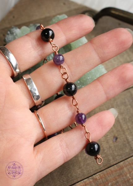 Copper wire wrapped bracelet features 8mm black tourmaline beads individually wrapped with 6mm amethyst beads individually wrapped linking together for an elegant bracelet. Showing the bracelet in hand as another perspective on craftmanship.