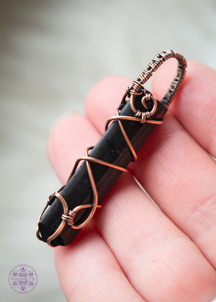 Black Tourmaline point wrapped in copper wire with a criss cross design up the front and a simple woven bail. This protection crystal is great for a minimalist and can be unisex. Held in hand showing the side and bail details.