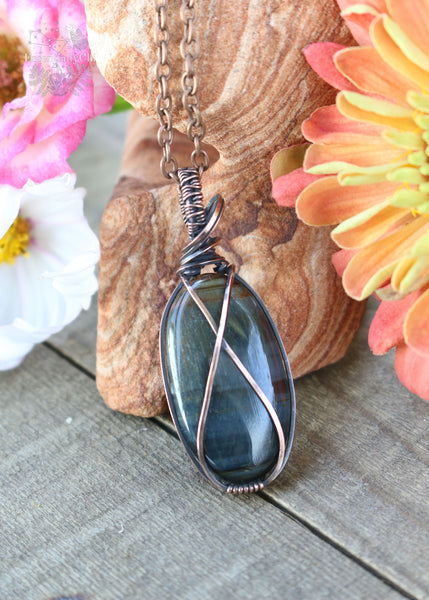 Bkue tiger eye oval pendant wrapped in copper wire with a criss cross shape across rhe face of the stone. 