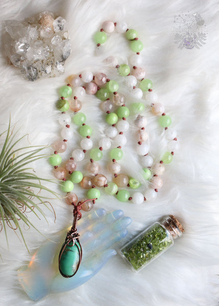 Embrace heart-centered healing with "The Heart Healer" Green Calcite & Chrysoprase Mala Necklace. Hand-knotted with green calcite, rainbow moonstone, and flower agate, it features a copper wire wrapped chrysoprase pendant. Slip it effortlessly over your head for mindful meditation, grounding, and heart chakra activation. Let this mala be your guide to self-love, aligning your heart with its true desires. Elevate your spiritual journey with this unique mala designed for emotional healing and love.
