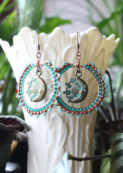 Celestial Beaded Boho Hoop Earrings featuring a turquoise, terra cotta, brass, and aqua green seed bead pattern. Brass sun and moon charm at the center of the 1.9-inch diameter hoops, hanging 2.5 inches from copper ear hooks. A cosmic expression of bohemian style