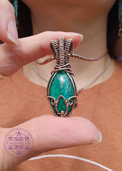 Chrysocolla in Bloom necklace in wire wrapped copper. Crystal is an oval shape with a copper wrapped petal shape at the bottom. Bail is an elegant layered look for depth. Shown in hand for size reference. 