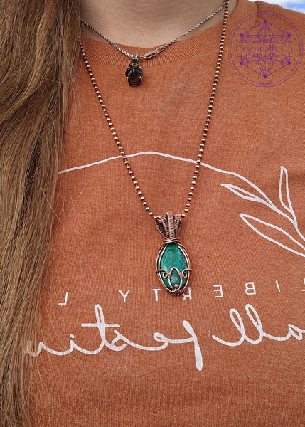 Chrysocolla in Bloom necklace in wire wrapped copper. Crystal is an oval shape with a copper wrapped petal shape at the bottom. Bail is an elegant layered look for depth. Shown worn around neck. 