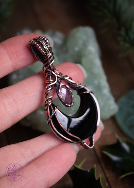 Lilith is a black onyx and faceted amethyst copper wire wrapped pendant. She's a black crescent moon facing upwards (curve side down) and above the moon is the faceted amethyst that captures the light. Shown in hand looking at the side foor further detail.