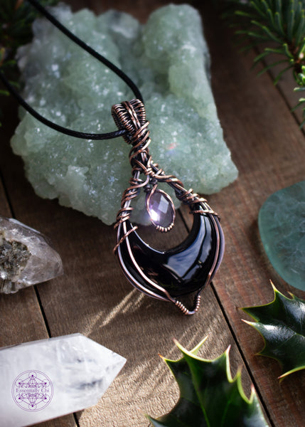 Lilith is a black onyx and faceted amethyst copper wire wrapped pendant. She's a black crescent moon facing upwards (curve side down) and above the moon is the faceted amethyst that captures the light. Shown laying against a prehnite crystal with the bright light shining thru the amethyst and the reflections and shadows just emphasize the meaning of this pendant.