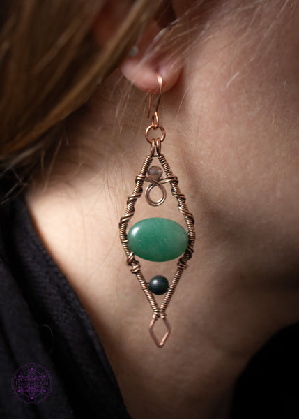 Mossy Spruce Earrings are Copper Wire Wrapped statement earrings in a diamond shape with an oval green aventurine crystal in the middle, moss agate at the bottom point and smoky quartz at the top point. Meant to represent the mossy Sitka Spruce trees in winter with the woodland creatures nestled in it's branches. Shown being worn for size reference. They hang about to the middle of my neck.