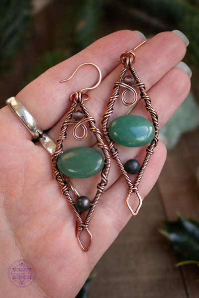 Mossy Spruce Earrings are Copper Wire Wrapped statement earrings in a diamond shape with an oval green aventurine crystal in the middle, moss agate at the bottom point and smoky quartz at the top point. Meant to represent the mossy Sitka Spruce trees in winter with the woodland creatures nestled in it's branches. Shown held in hand for size reference. These earrings have some weight to them.