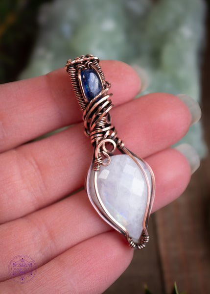 This Rainbow Moonstone and Blue Kyanite necklace is wrapped in copper wire with a teardrop moonstone pointing down, reflecting a rainbow flash off the facets of the stone. The bail has a brilliant dark blue kyanite and swirls around the bail like winter winds whirling around the snow. This pendant reminds me of a fresh blanket of snow on a cloudless winter night.  Shown in hand for size reference.