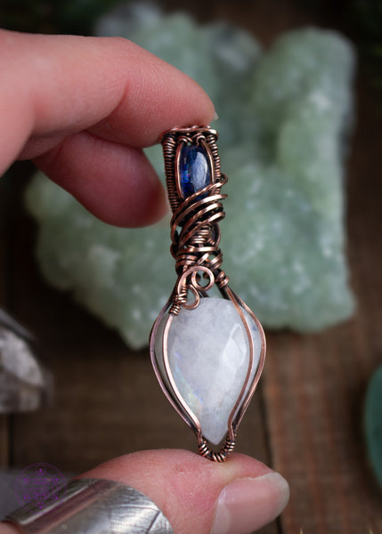 This Rainbow Moonstone and Blue Kyanite necklace is wrapped in copper wire with a teardrop moonstone pointing down, reflecting a rainbow flash off the facets of the stone. The bail has a brilliant dark blue kyanite and swirls around the bail like winter winds whirling around the snow. This pendant reminds me of a fresh blanket of snow on a cloudless winter night. 